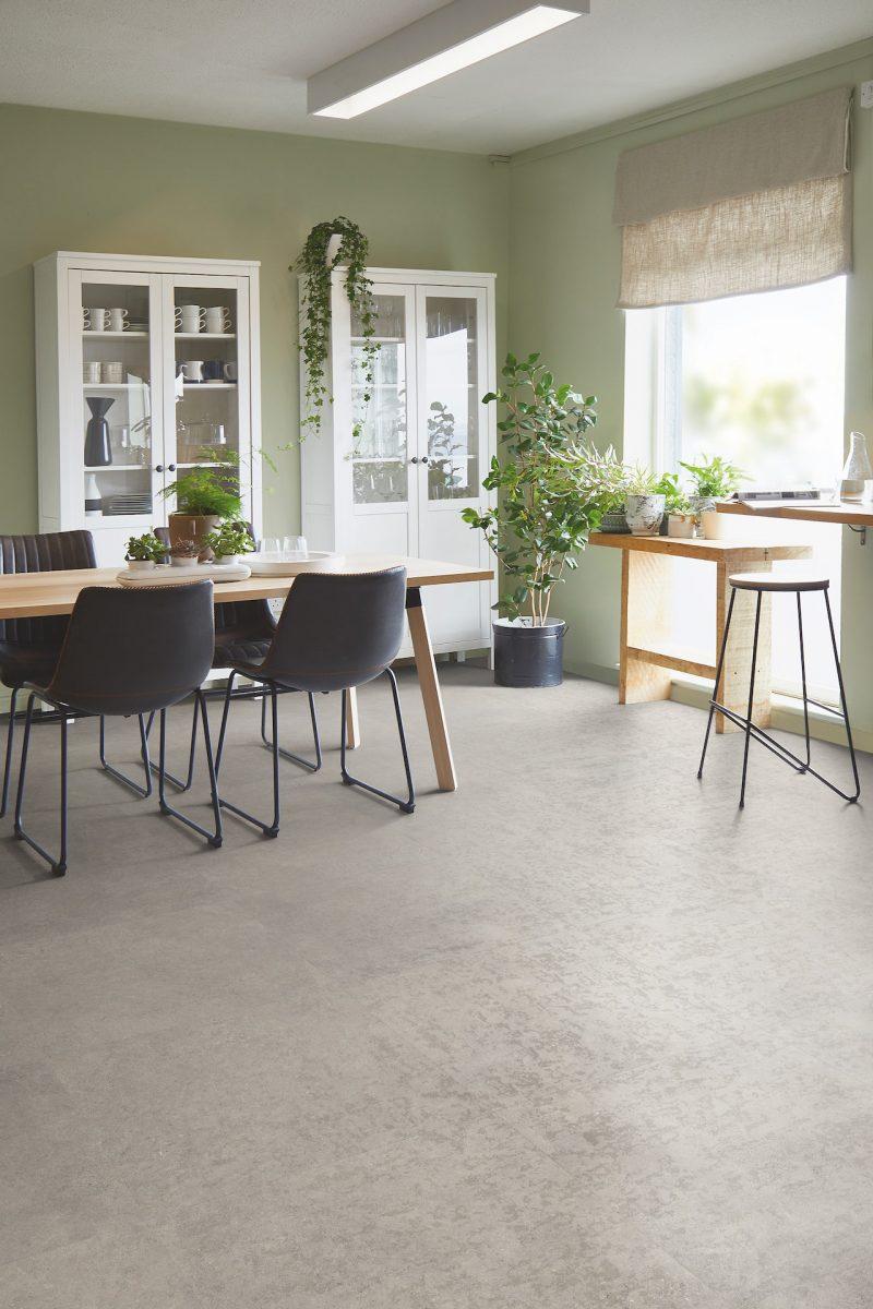 A modern dining room featuring newly installed light grey stone-effect luxury vinyl tile (LVT) flooring with sage green walls and white furniture.