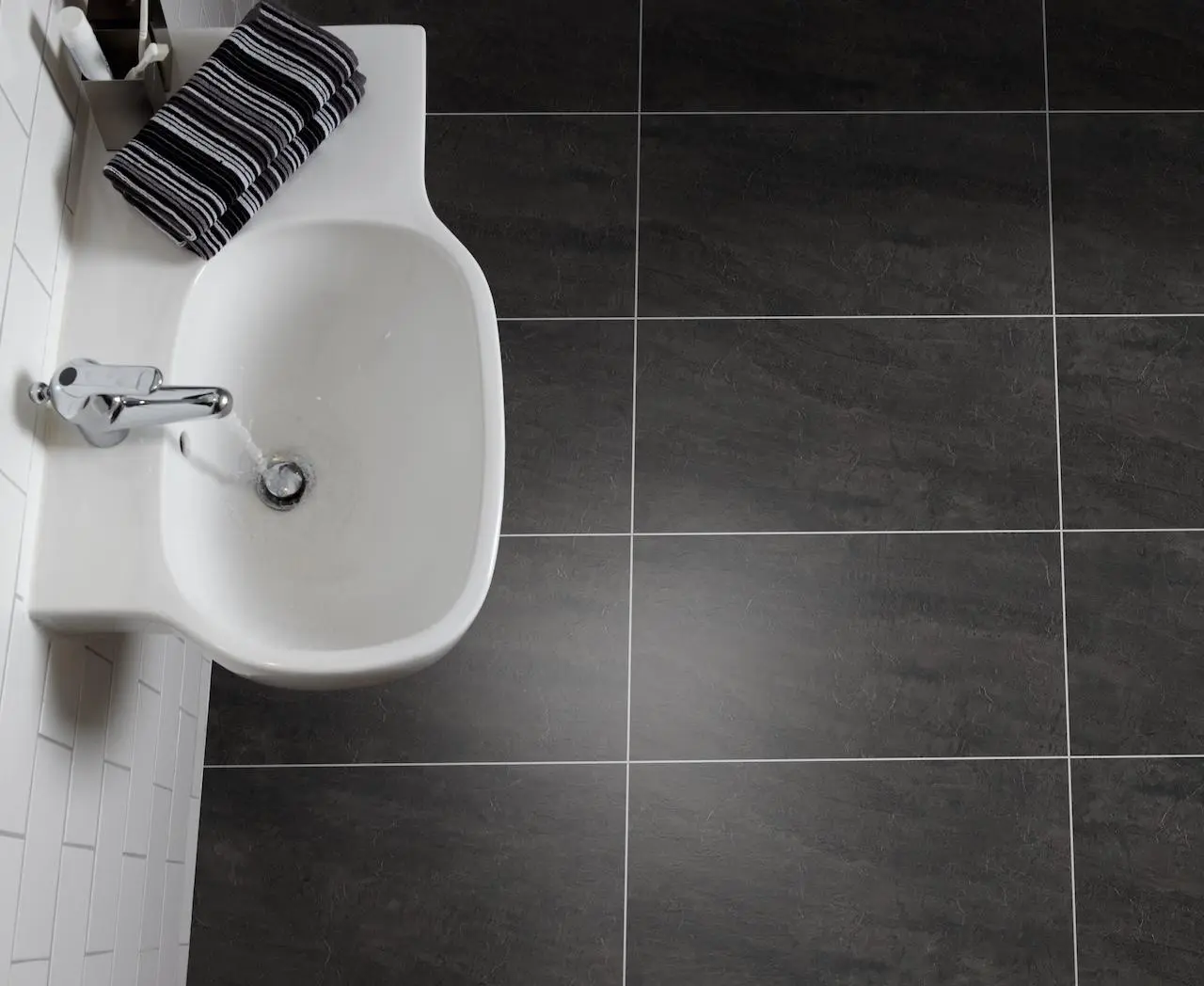 Polyflor Colonia Welsh Raven Slate LVT: Durable Slate Effect Bathroom Flooring Dark grey slate effect Luxury Vinyl Tile (LVT) flooring from the Polyflor Colonia range in Welsh Raven Slate, laid in a bathroom next to a white sink.