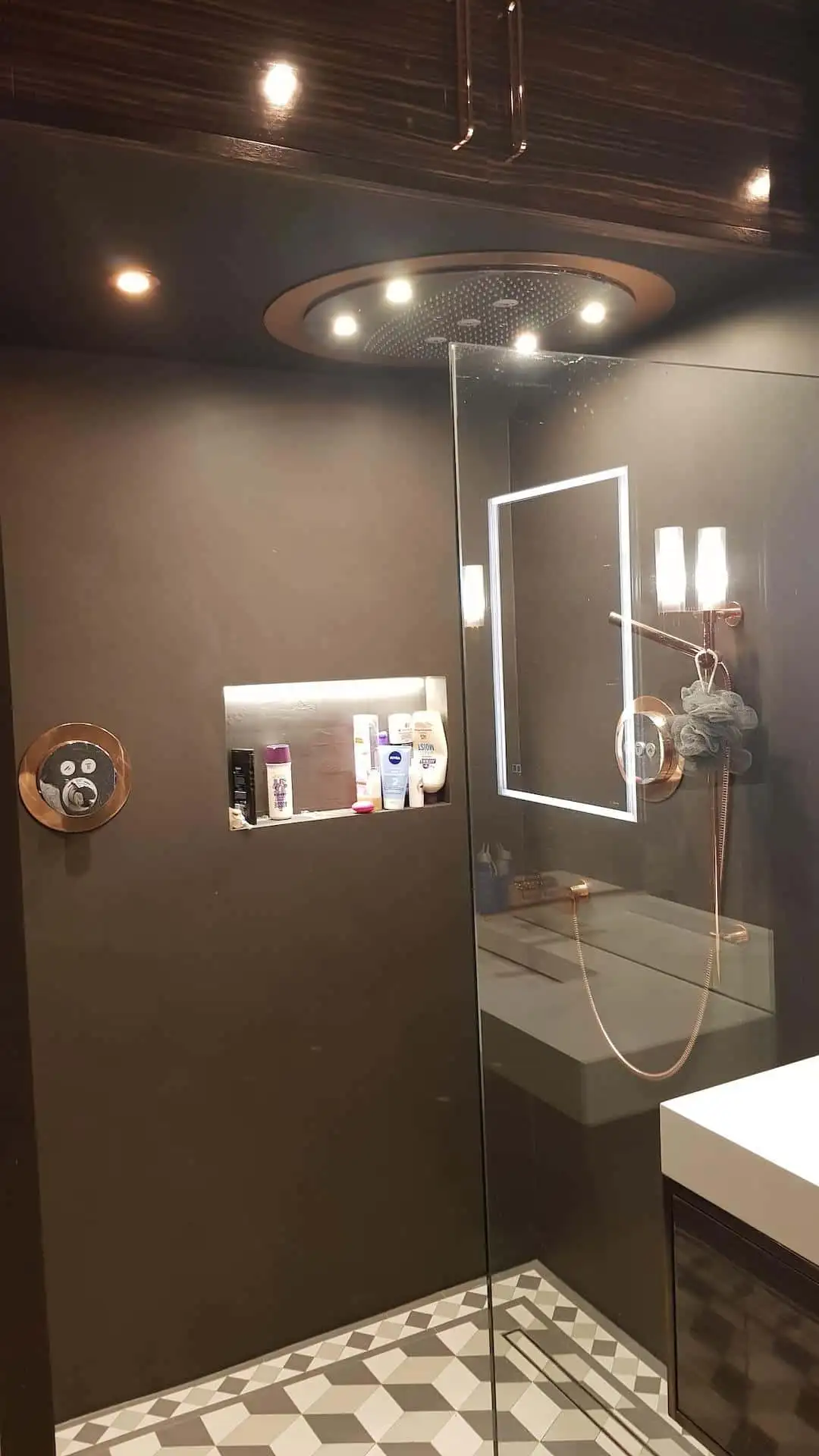 Luxury Dark Microcement Walls with Rose Gold Fixtures and Patterned Floor Dark, seamless microcement shower walls and ceiling paired with a geometric patterned tiled floor and contrasting rose gold/copper shower fixtures in a luxury wet room.