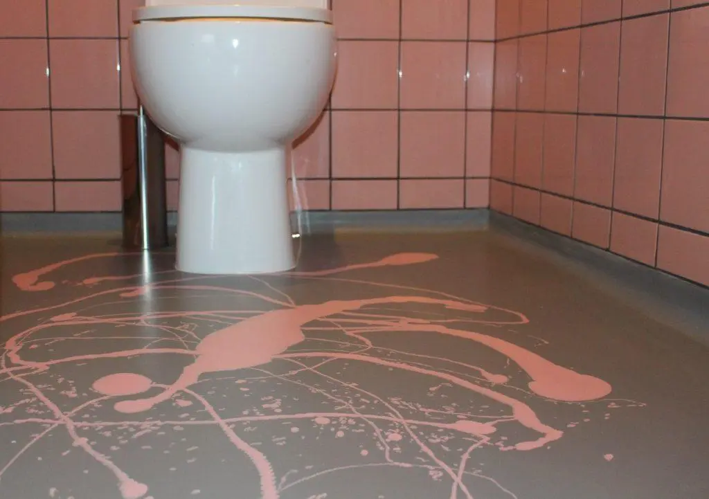 Bespoke Pink Splatter Resin Bathroom Flooring: Seamless & Waterproof Seamless grey resin bathroom floor with a bold, bespoke pink splatter design around a white toilet, ideal for modern wet rooms and artistic interiors.
