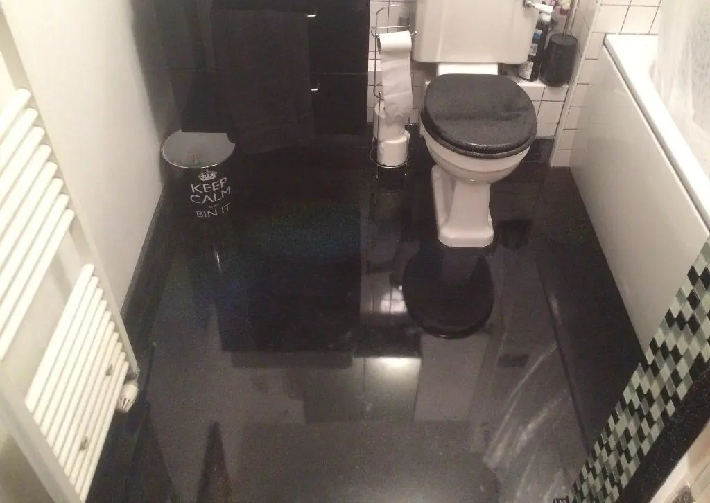 High-Gloss Black Resin Bathroom Floor: Seamless, Striking & Waterproof Seamless high-gloss black resin floor in a modern bathroom with a white toilet and black storage, emphasizing the reflective, waterproof epoxy finish.